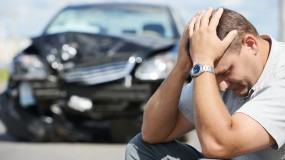 Mand sidder med hovede i hænderne efter ulykke med bils som er totalskadet