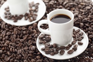 To kaffekopper med kaffe omgivet af kaffebønner